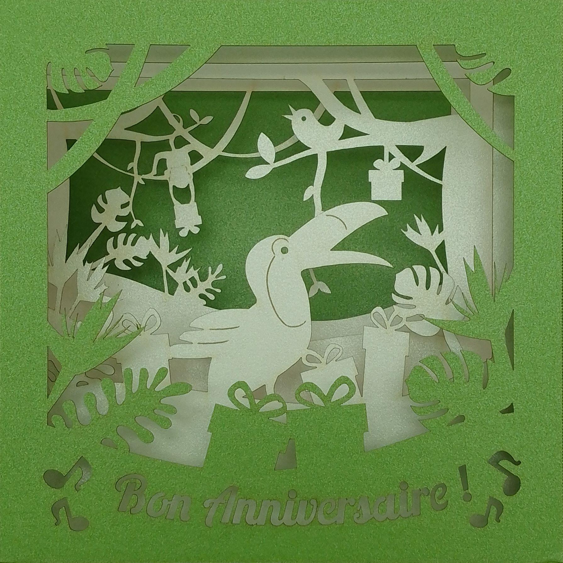 Carte 3D d’anniversaire représentant un cacatoès entouré de cadeaux dans une ambiance jungle, haut de gamme 300g, confectionnée artisanalement à Embrun.